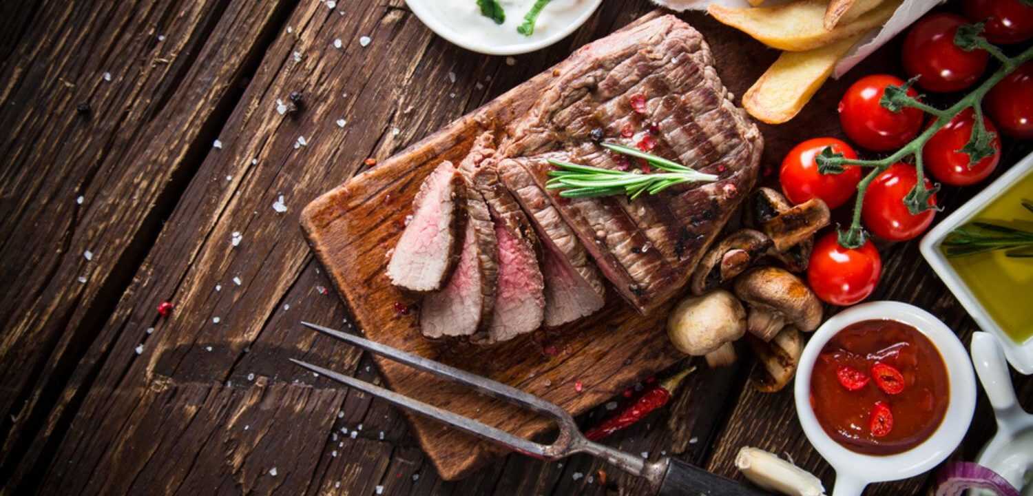 A mouthwatering steak on a wooden cutting board garnished with fresh tomatoes and garlic.